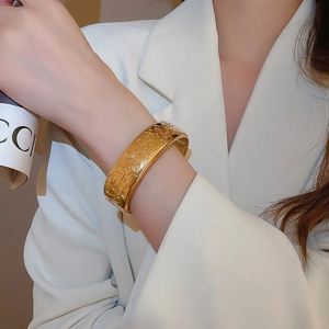 Close-up of golden wide cuff bracelet with vintage floral engraving on model's wrist