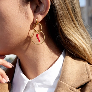 Gold multi-hoop earrings with red chili pepper pendant worn in a stylish outdoor setting