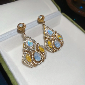 Close-up of teardrop zirconia crystal earrings with blue opal and gold plating