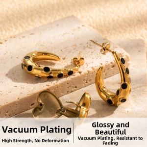 Detail of gold C-shaped earrings with black heart pendant on a stone background
