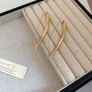 Macro detail of elegant gold-plated streamlined S-curve drop earrings with polished finish