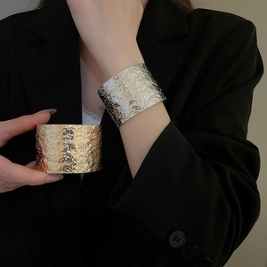 Detailed view of wide irregular hammered metal cuff bracelets in gold and silver finish