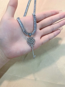 Close-up of silver key pendant necklace with baguette zircon chain on yellow silk