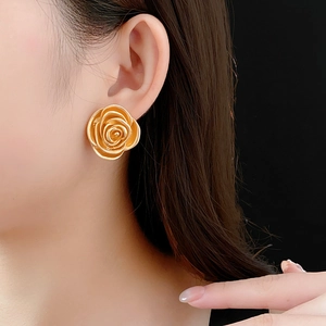 Close-up of a vintage golden rose earring worn by a model against a black background