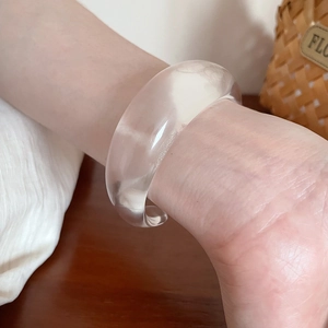 Close-up of a wide transparent acrylic bangle on a wrist with a retro aesthetic background
