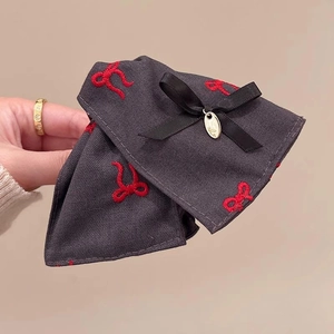 Detail of dark grey twill bow hair clip with red embroidery and golden metal tag