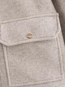Nahaufnahme der Tweed-Stoffstruktur mit goldenem Metallknopf und Klapptaschen-Detail