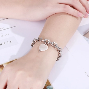 Detail eines klobigen Edelstahl-Kettenarmbands mit einem weißen Herzanhänger aus Muschel