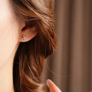 Close-up of elegant silver cross stud earrings with sparkling cubic zirconia on ear