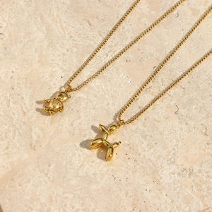 Detail of 18K gold-plated balloon dog and bear pendants on fine chains over stone surface