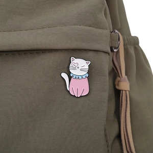 Cute cartoon cat enamel pin with blue collar and pink heart on green backpack