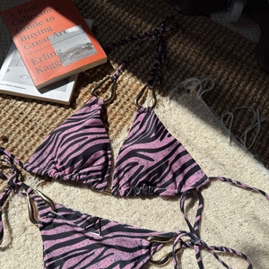 Detail of pink zebra print bikini with large decorative gold rings on straw mat