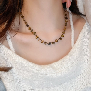 Détail d'un collier de perles irrégulières en oeil de tigre sur pull blanc