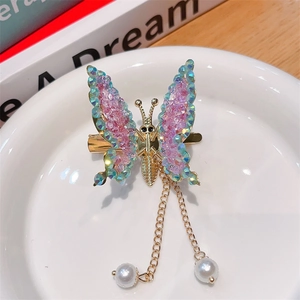 Detail of golden butterfly hair clip with colorful rhinestones and white pearl tassels