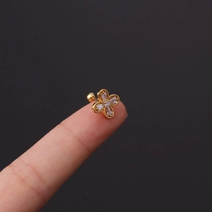 Macro shot of a tiny gold flower cartilage stud with zircon petals held on a fingertip