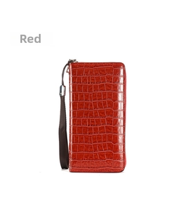 Detail einer roten Brieftasche mit Krokodilstruktur, Reißverschluss und gewebter Handschlaufe
