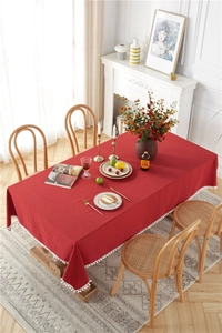 Detail of red cotton tablecloth featuring white pom-pom fringe on a wooden dining table