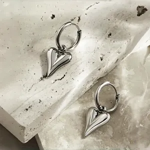 Boucles d'oreilles créoles avec pendentif cœur argenté poli sur une surface en pierre