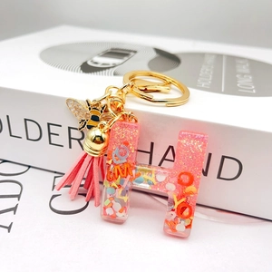 Macro detail of resin letter H keychain with pink glitter and gold bee charm