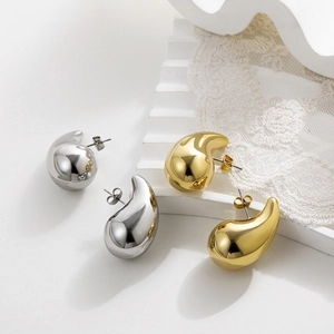 Detail of teardrop stud earrings in gold and silver finish on elegant white lace background