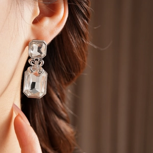 Close-up of silver square gemstone drop earrings with bow detail worn by a model