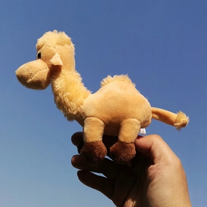 Detailed view of a tan camel plush keychain held against a bright blue sky background