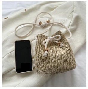 Mini woven straw bucket bag shown next to a smartphone to demonstrate its portable size