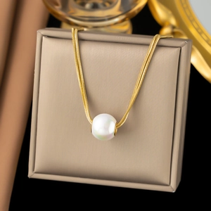 Elegant gold snake chain necklace featuring a large white pearl pendant on a beige box