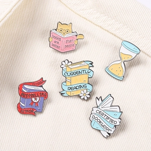 Cute cat and book enamel pin set on denim fabric featuring currently reading text