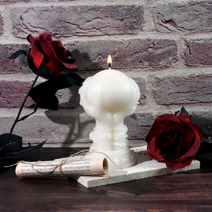 Close-up of lit skull hand bouquet candle with rose and parchment for gothic decor
