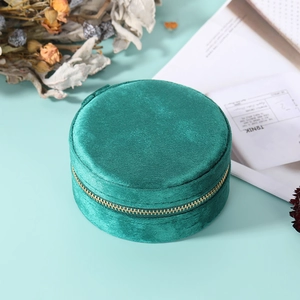 Detail of round dark green velvet jewelry box with gold zipper on a minimalist setting