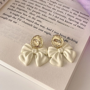 Detailed shot of cream bow earrings with golden discs on a vintage English book