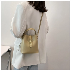 Beige bucket bag shown on shoulder with adjustable strap and metal lock closure