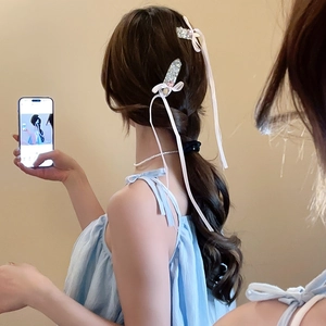 Close-up of hair clip featuring cream ribbon bow with sparkling rhinestones on model