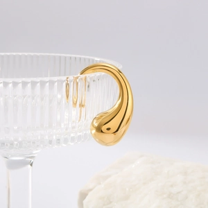 Elegant gold teardrop earrings in polished stainless steel hanging on a glass rim