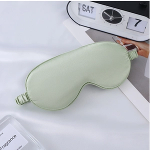 Detail of light green satin sleep mask with elastic strap on white fabric background