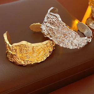Dettaglio dei bracciali a polsino in oro e argento con texture a pieghe irregolari
