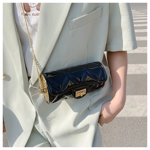 Detail of a black quilted cylindrical bag with a gold chain and pearl clasp decor