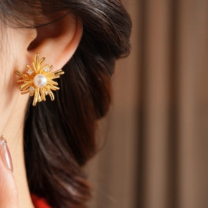 Close-up of gold sunburst stud earring with a central white pearl and sparkling crystals