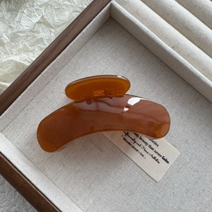 Close-up of a glossy amber hair claw clip inside a wooden box with linen fabric