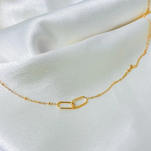 Macro view of interlocking oval links on a gold beaded chain necklace over white silk