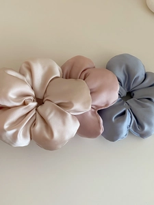 Detailed view of three satin scrunchies in champagne, dusty pink, and grey-blue colors