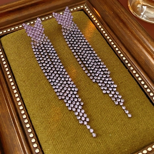 Vue détaillée de longues boucles d'oreilles à pompons violets sur velours vert