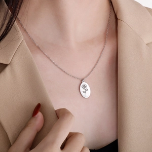 Close-up of a silver oval pendant with detailed rose engraving on a delicate chain