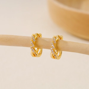 Detail of gold-plated twisted huggie earrings with sparkling cubic zirconia on wood bar