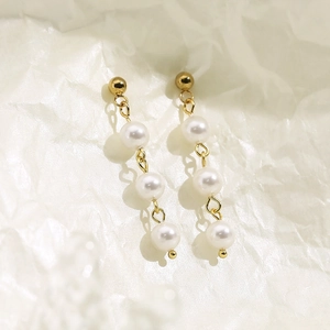 Détail de boucles d'oreilles dorées avec trois perles d'eau douce blanches graduées