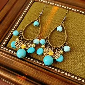 Detailed view of vintage gold bamboo earrings with turquoise beads on green fabric