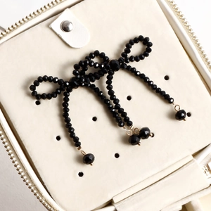 Detail of handcrafted black faceted bead bow earring with gold accents in a jewelry box