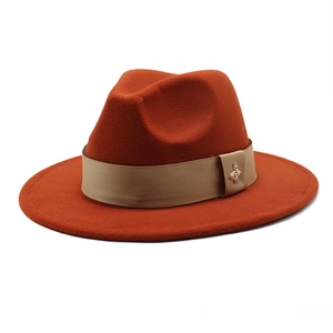 Close-up of rust red wool fedora hat featuring a gold bee emblem on a beige ribbon band