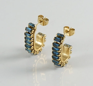 Detailed macro view of gold C-shape earrings featuring baguette-cut dark blue stones
